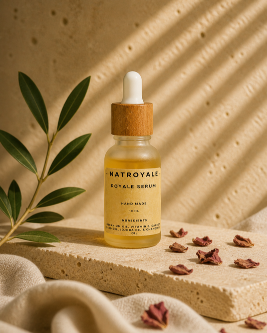 Royale Serum by Natroyale — lightweight botanical face serum in a frosted glass bottle with bamboo dropper, on a travertine stone shelf with olive branch and dried rose petals.